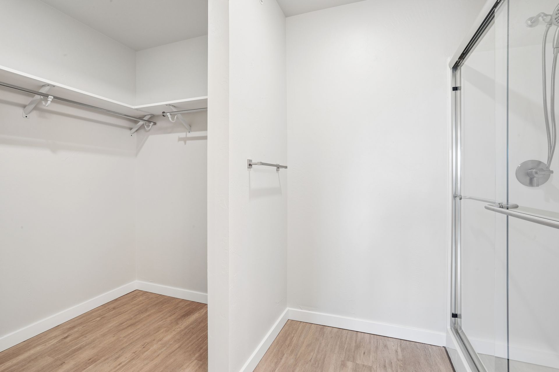 Empty white walk-in closet with wood floor and a glass shower door on the right