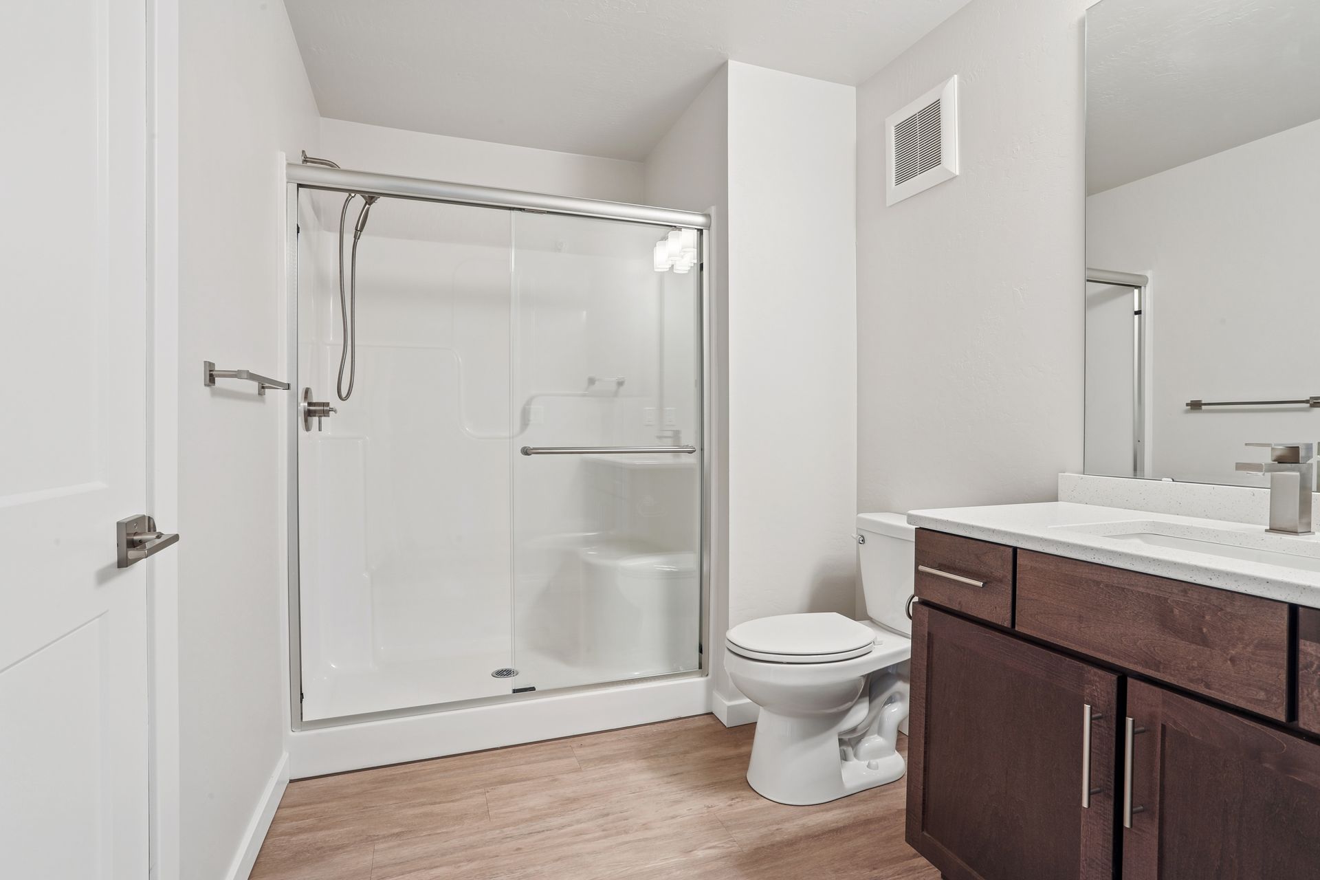 Bathroom with white shower, toilet, and dark wood vanity on light wood floor.