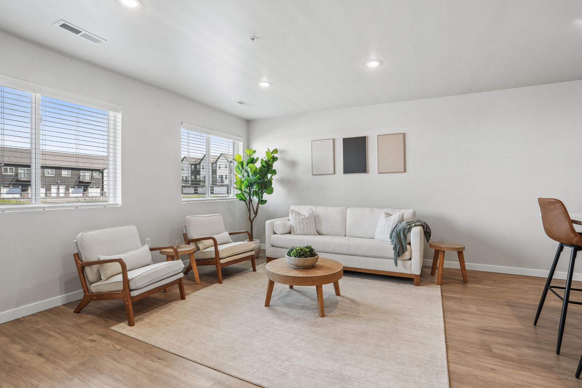 Bright modern living room with white sofa, two chairs, coffee table, rug, wall art, and bar stools by the window