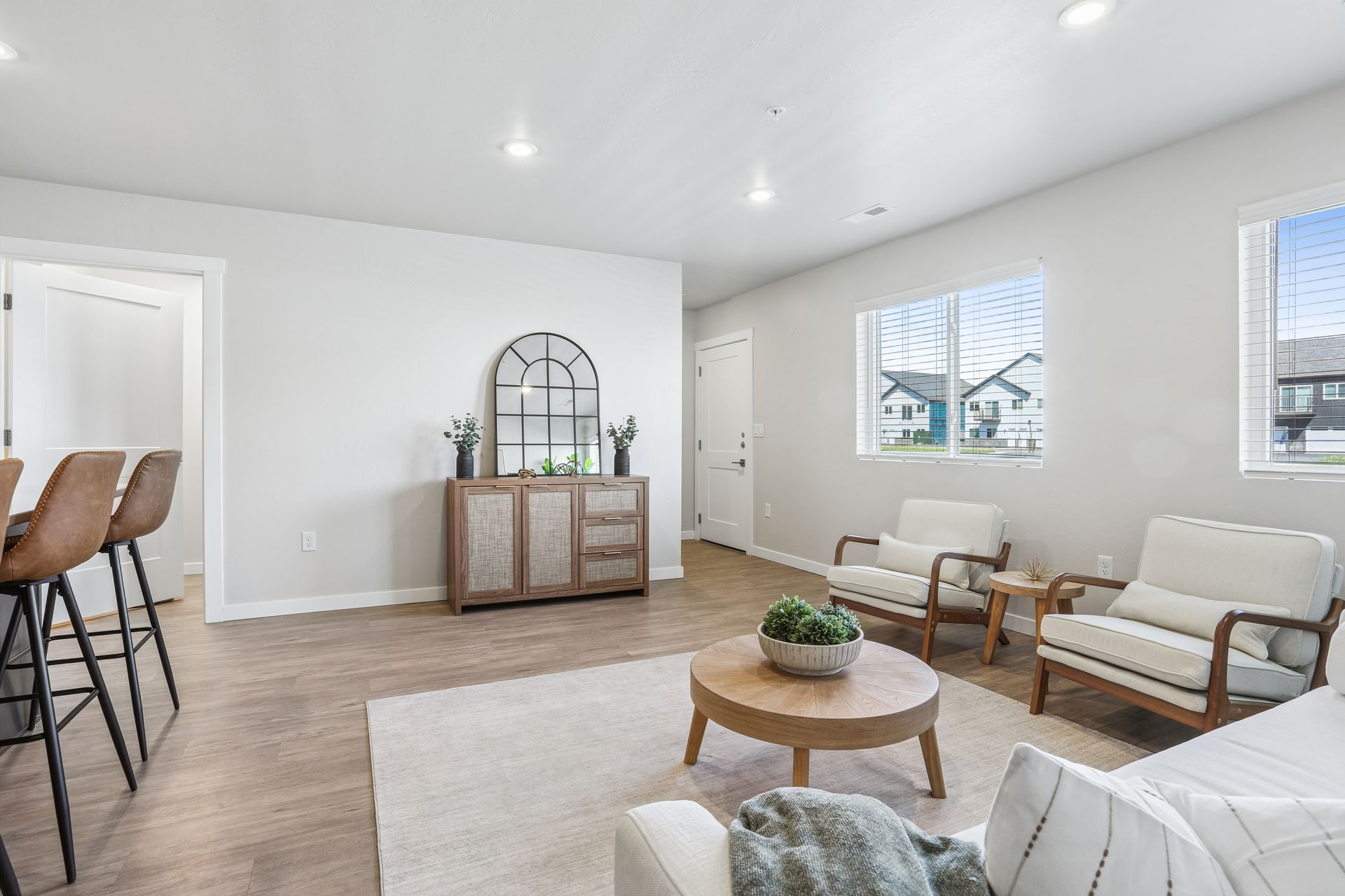 Bright modern living room with white walls, tan sofa, round coffee table, and bar stools by the doorway