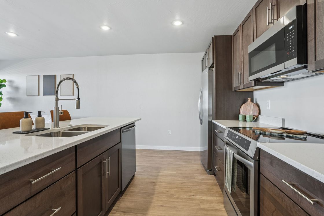 Modern kitchen with dark wood cabinets, stainless appliances, and a white island counter.