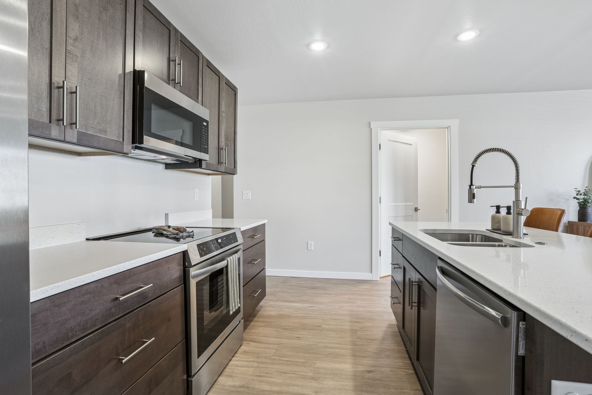 Modern kitchen with stainless steel appliances, dark cabinets, white walls, and an island sink