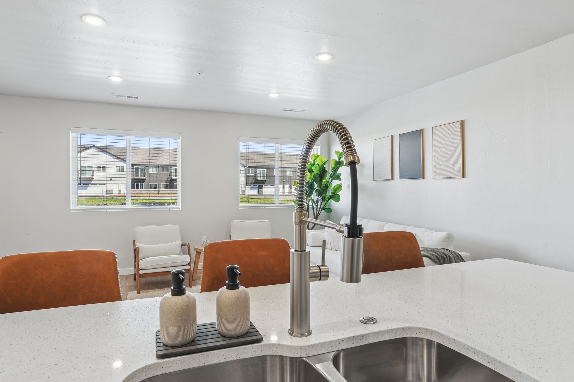 Bright modern kitchen with white island, sink faucet, orange chairs, and a sitting area by large windows