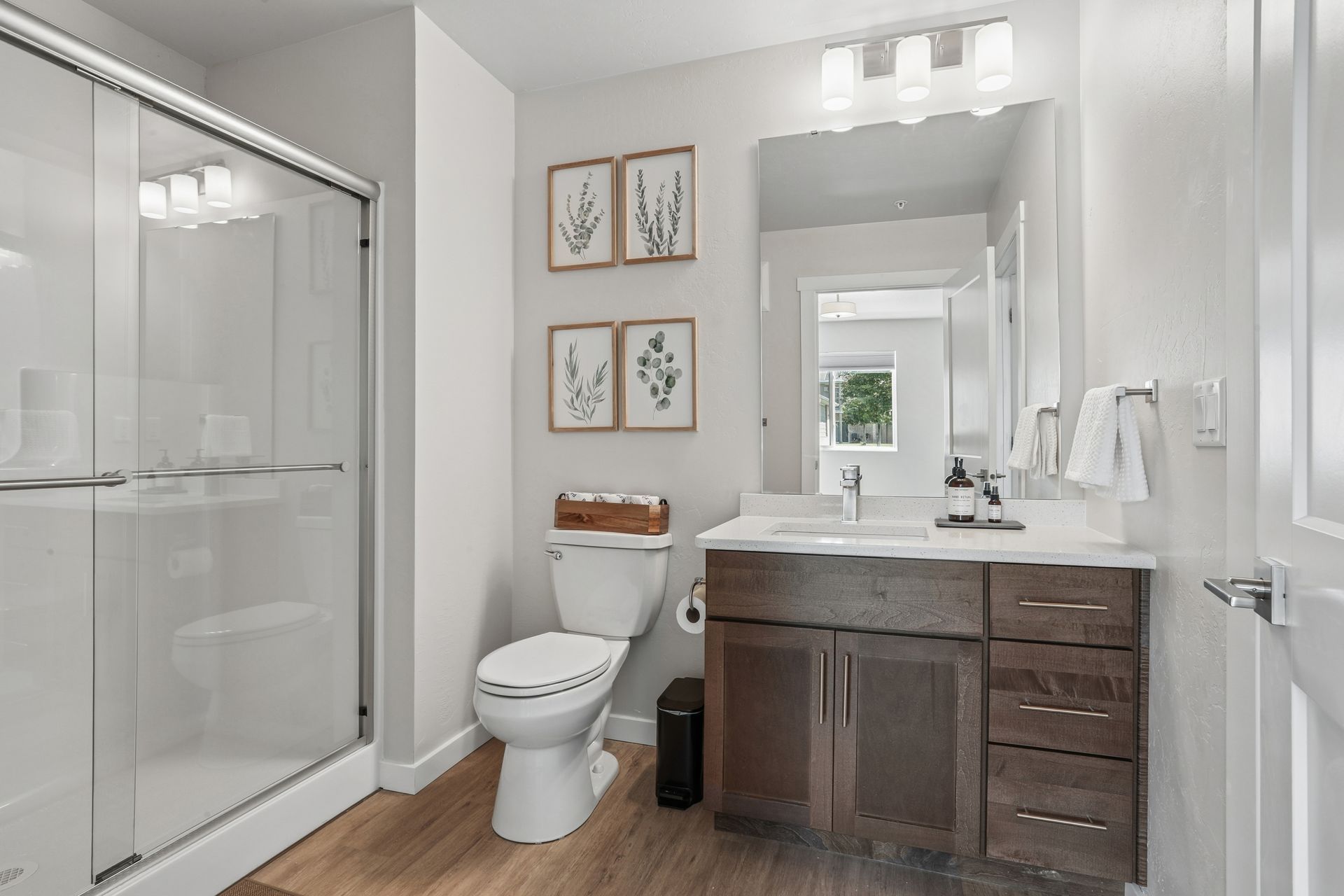 Bright modern bathroom with glass shower, toilet, vanity, and wall art.