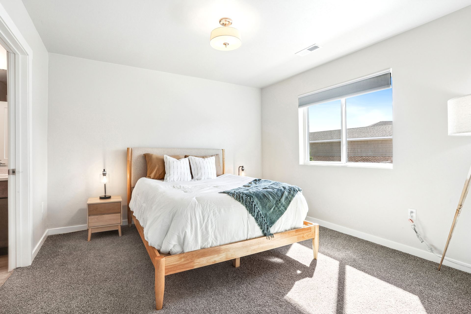 Bright bedroom with white walls, gray carpet, wooden bed, and sunlight from a window