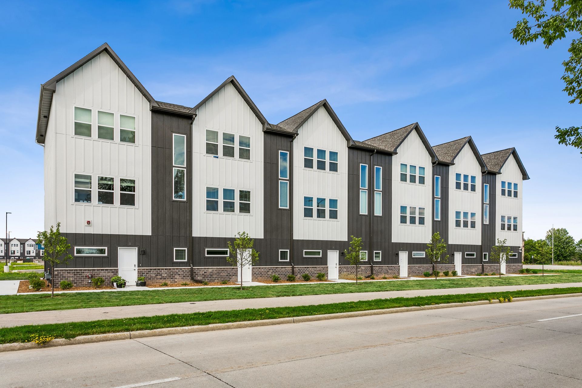 Row of modern white townhouses with dark trim along a street under a clear blue sky