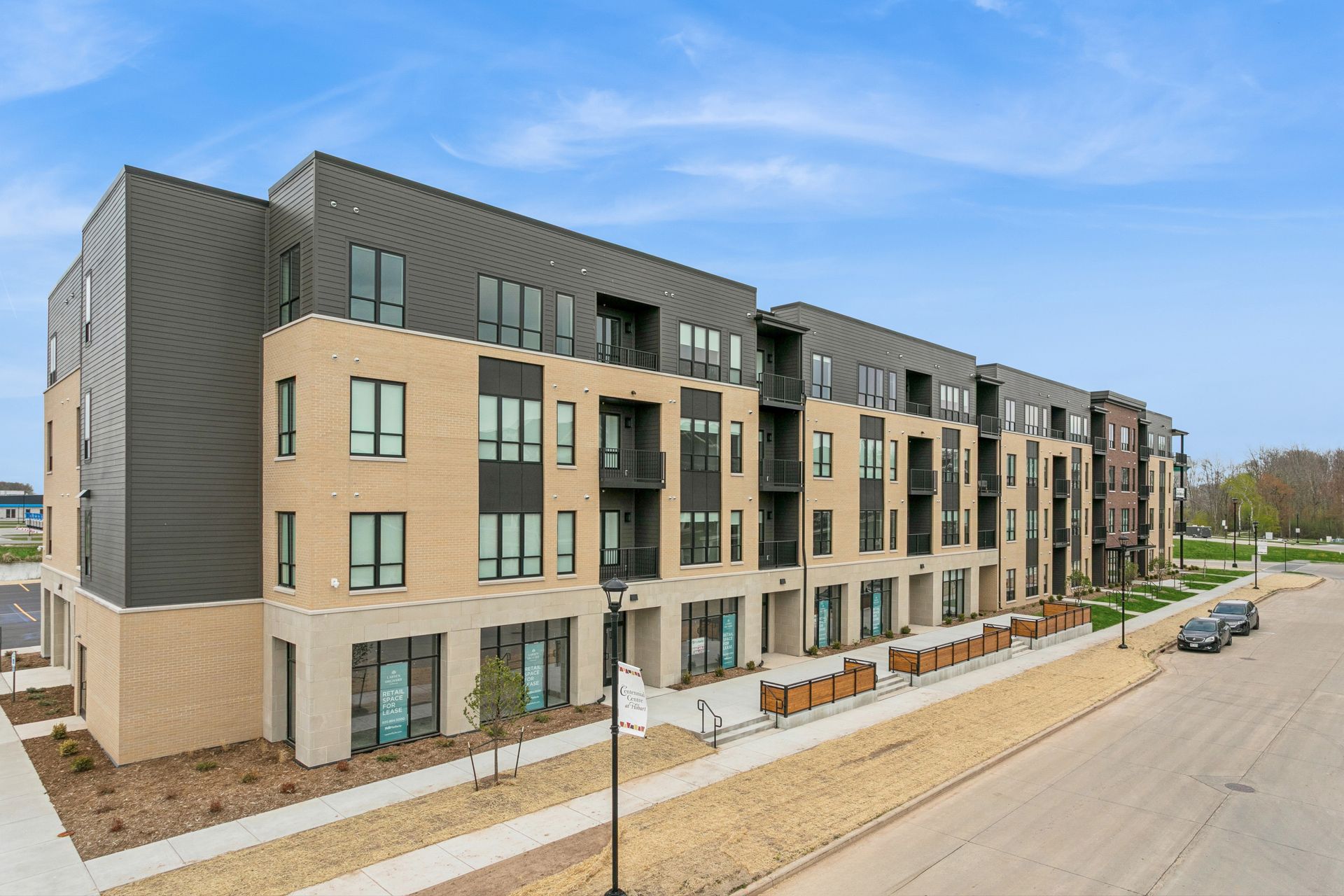 Modern four-story apartment building with balconies and a street in front under a blue sky