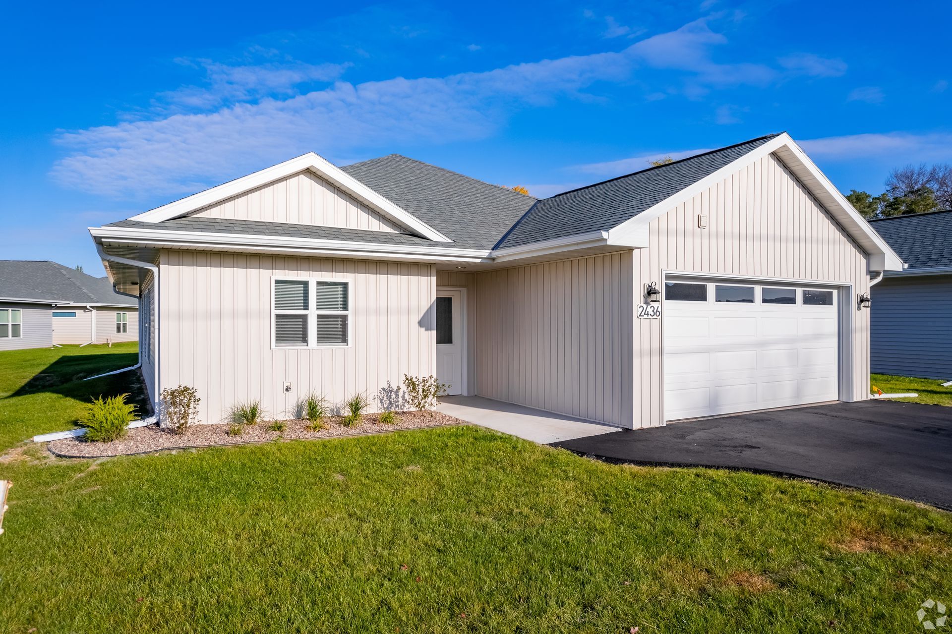 White single-story suburban house with a two-car garage, blue roof, and green lawn under a clear sky