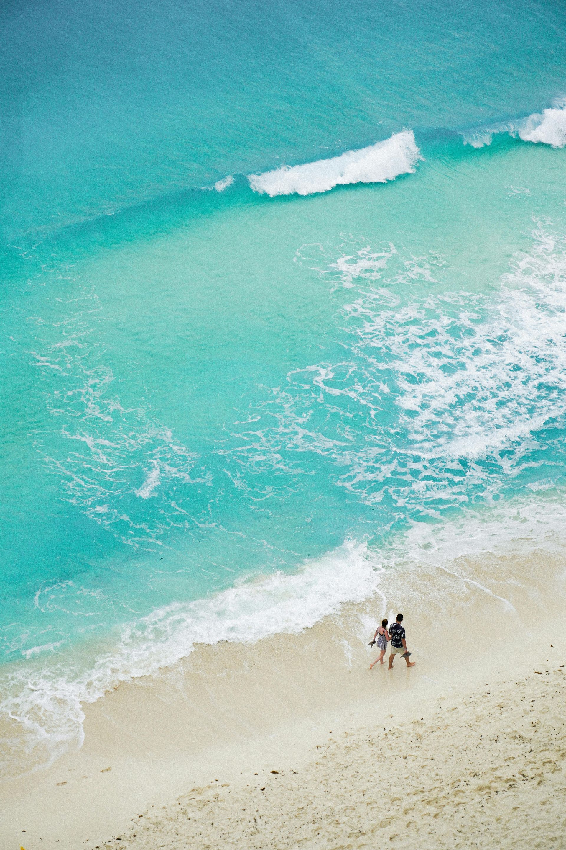 couple walking on an isolated beach in Caribbean with waves lapping against the white sand