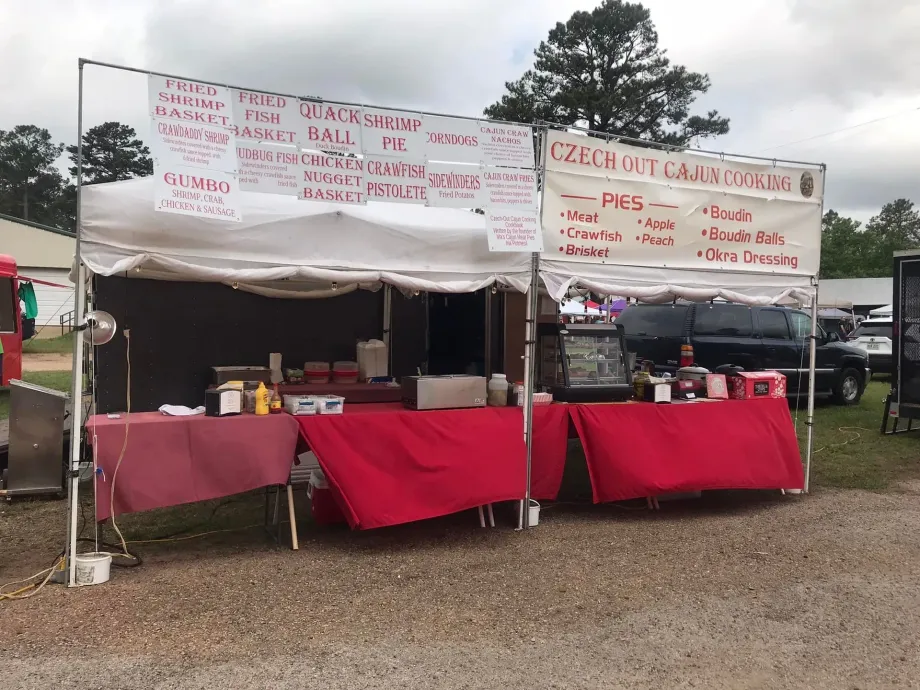Two red-covered food booths with white canopies at an outdoor market on a gravel lot.