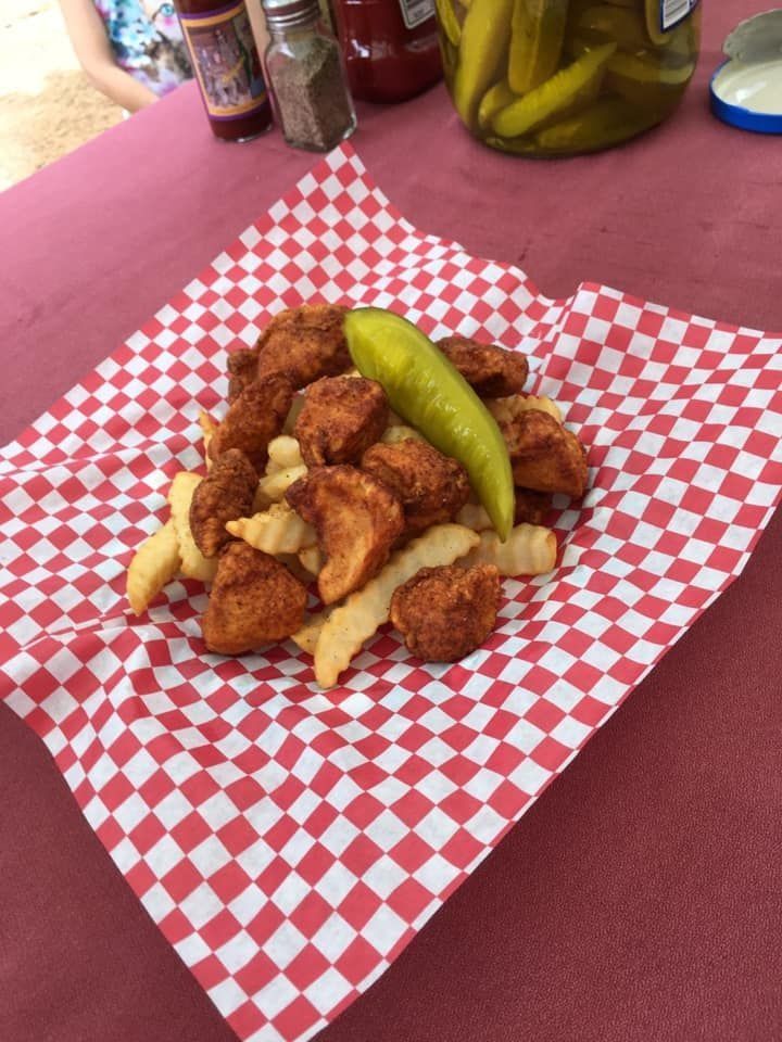 French fries and fried bites on red-and-white checkered paper with a pickle on top, on a pink tablecloth
