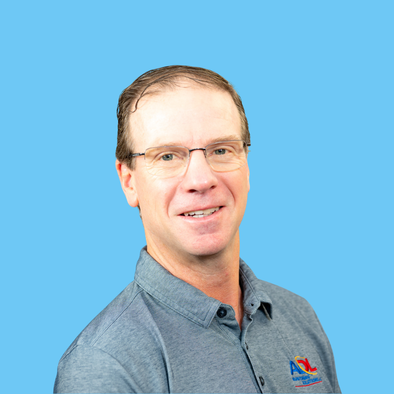 Man with glasses smiling, wearing a blue shirt. Background is light blue.