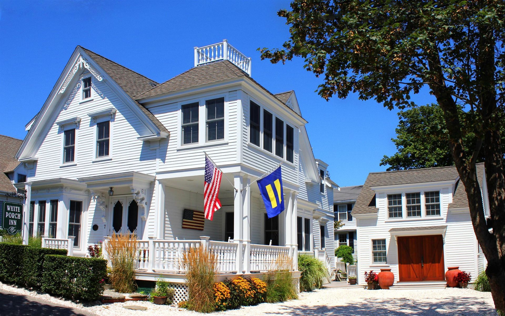 Exterior picture of the main house with front porch and carriage house with garden in front of it.