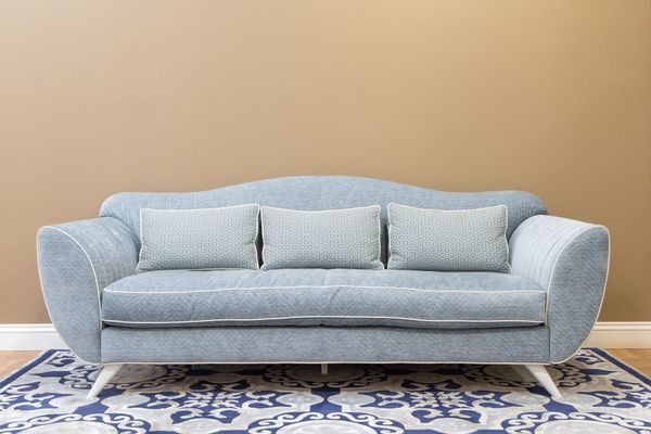 Light blue sofa with patterned pillows on a blue-and-white rug against a tan wall