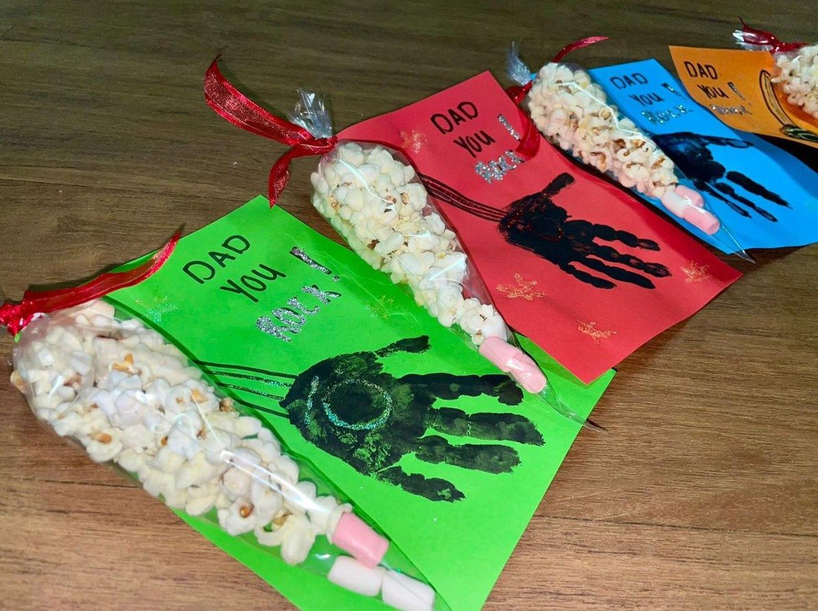 Colorful paper bags with handprint art and popcorn snacks tied with ribbons, saying