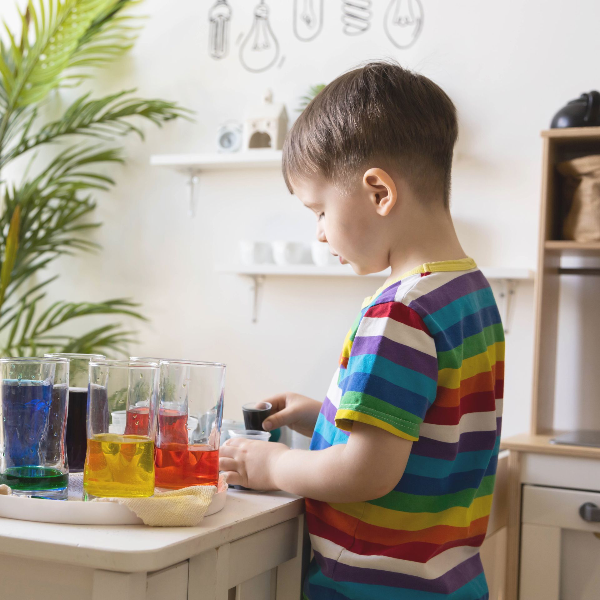 Young child with colorful shirt playing with colored liquids in glasses.