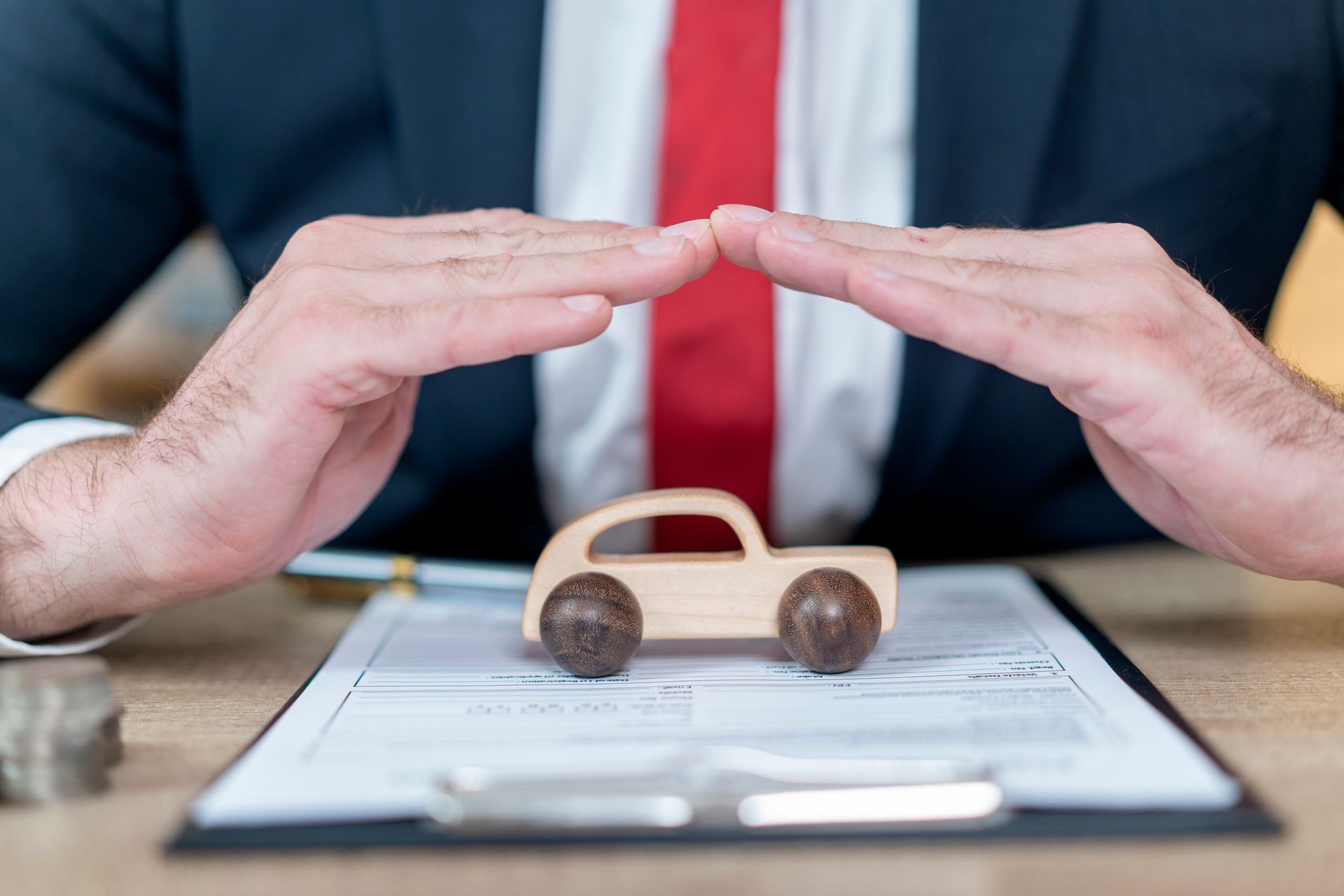A businessman covering a toy car with his hands, symbolizing vehicle insurance protection and care.