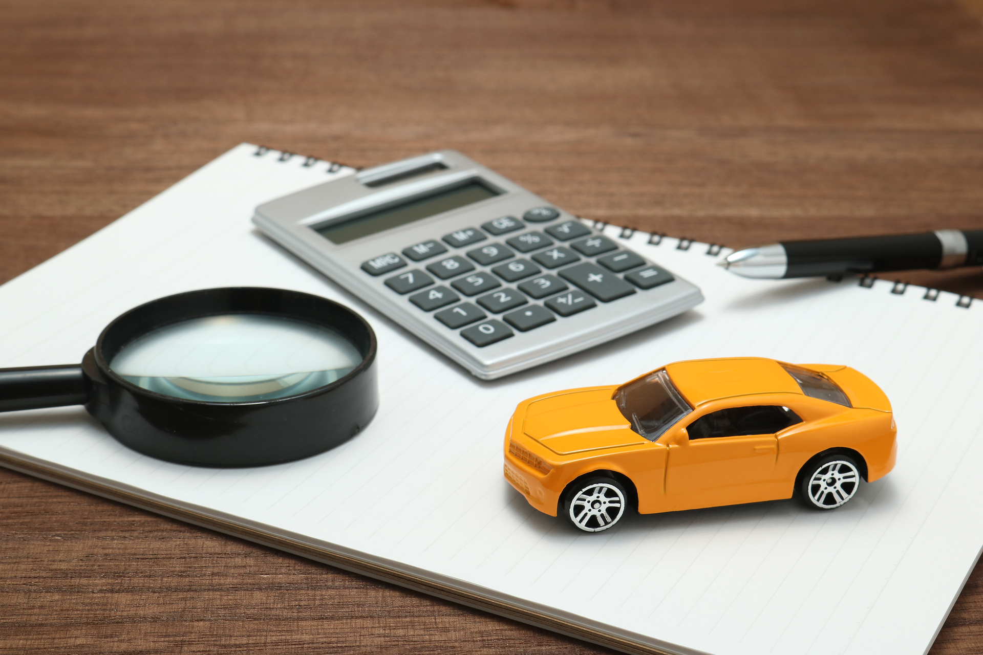 Items on a desk showcasing auto insurance calculations with toy car, calculator, and notebook.