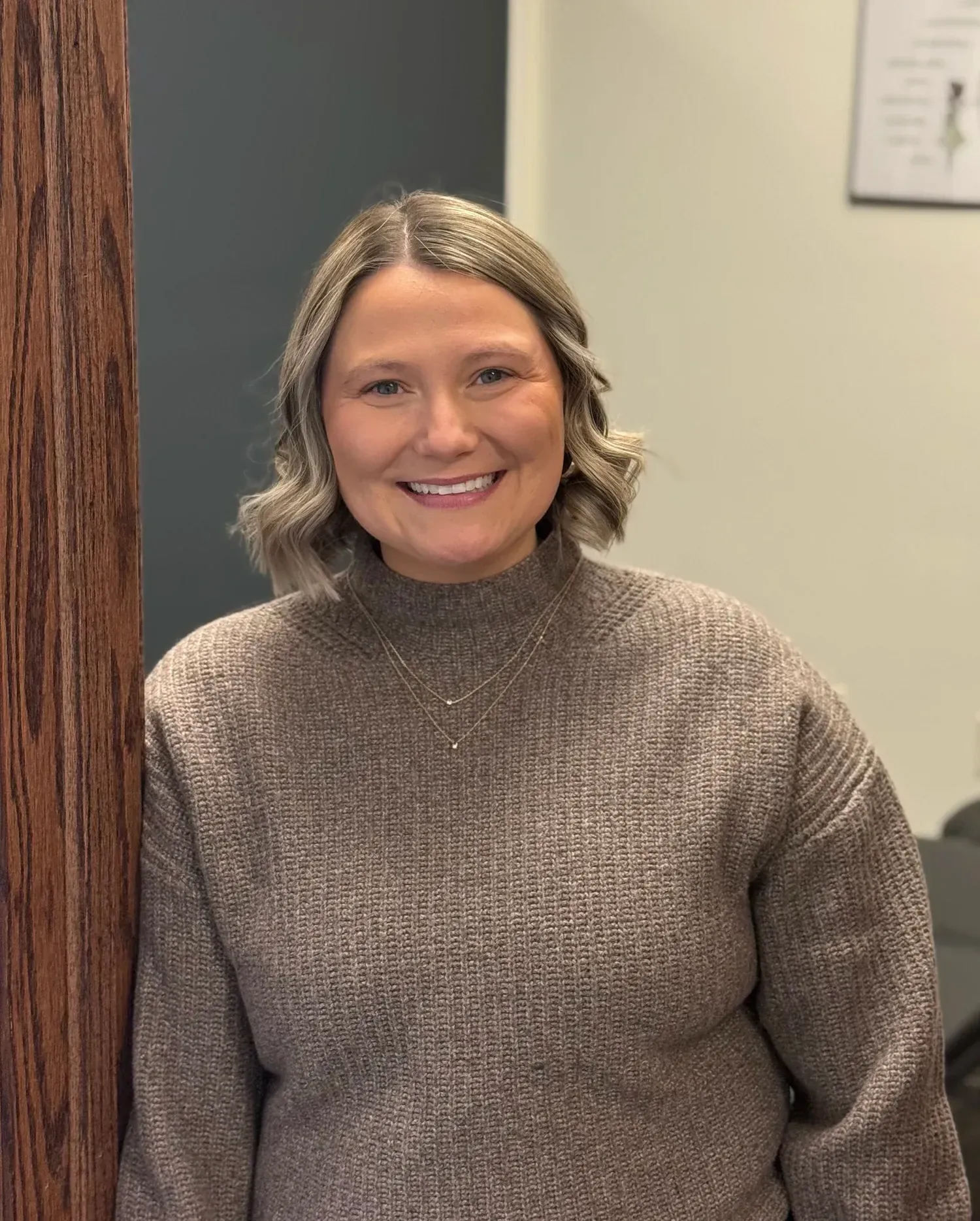 Smiling woman in a gray sweater standing indoors in an office setting