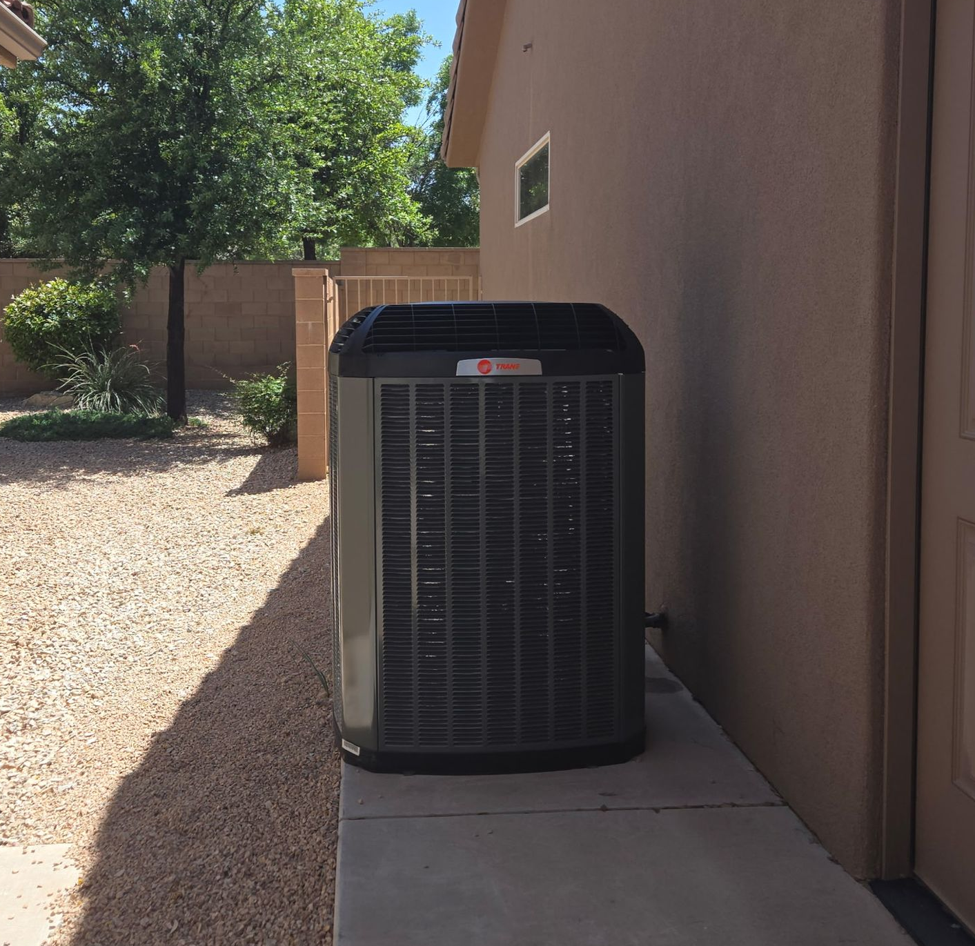 Outdoor air conditioning unit beside a beige house wall on a gravel patio.