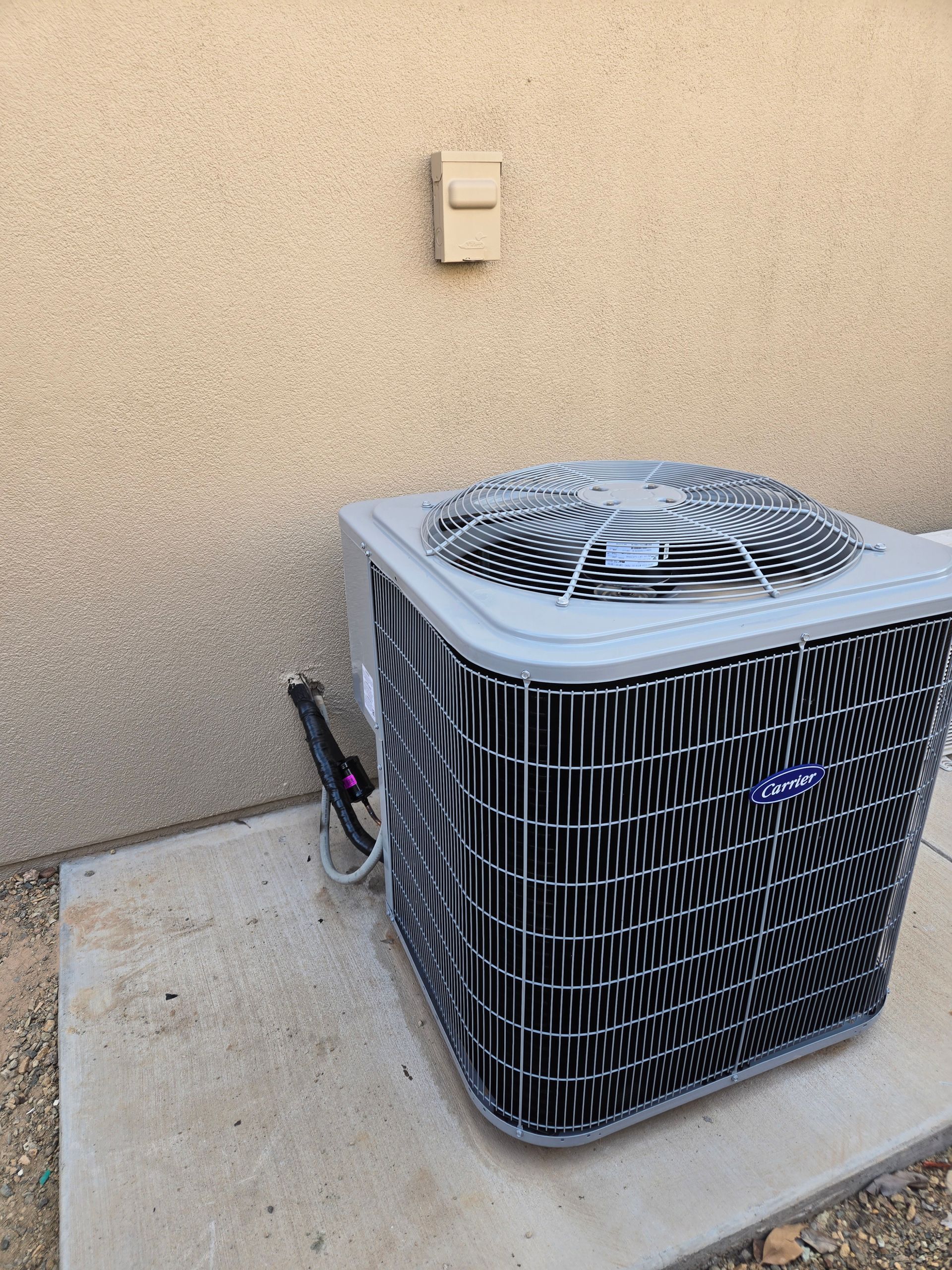 Outdoor air conditioner unit beside a beige stucco wall on a concrete pad.