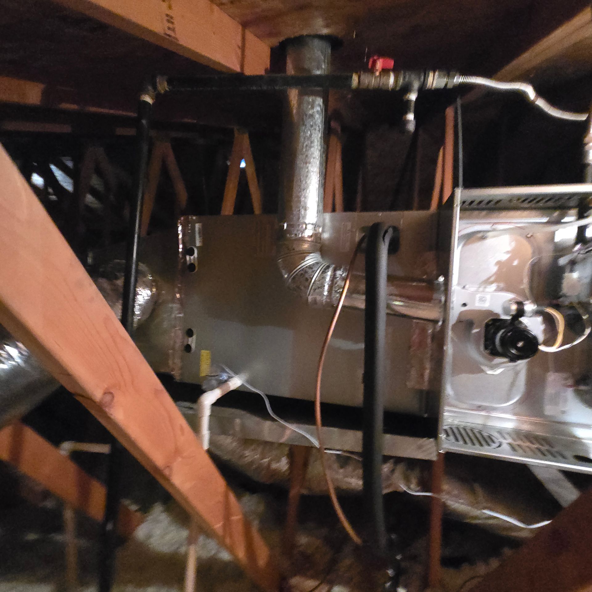 Attic HVAC unit with insulated ductwork and exposed wooden beams, dimly lit.