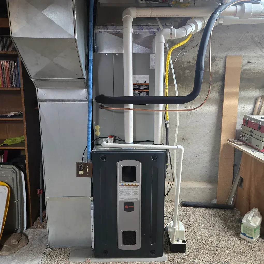 Basement furnace with ductwork, pipes, and a black vent hose against a concrete wall