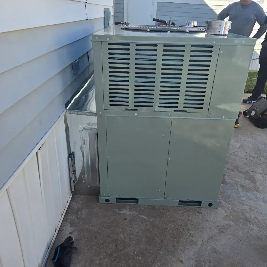 Outdoor HVAC unit beside a house wall on a concrete slab, with a person partially visible in the background