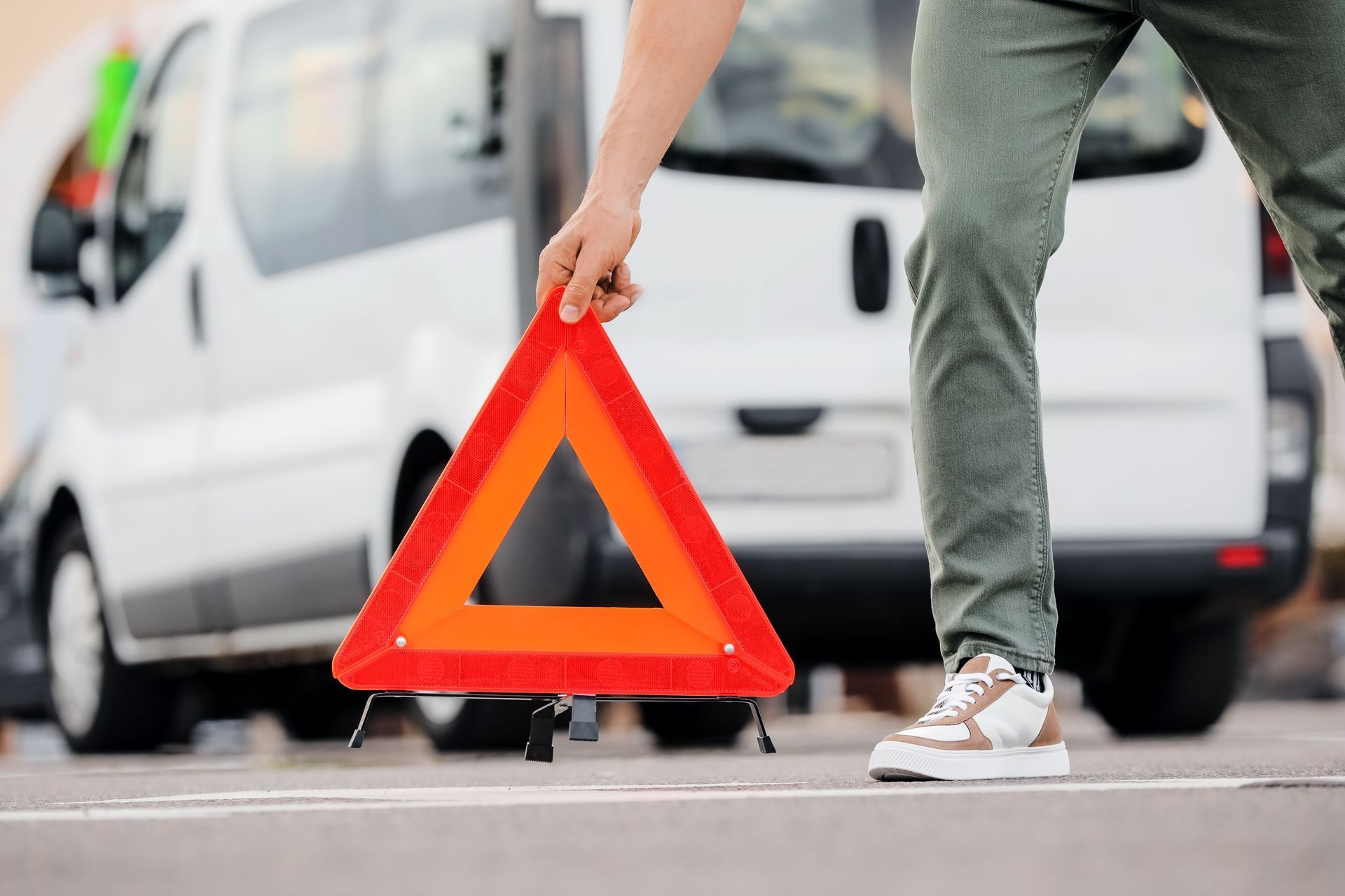 Persona che regge un triangolo di segnalazione rosso accanto a un furgone bianco su una strada
