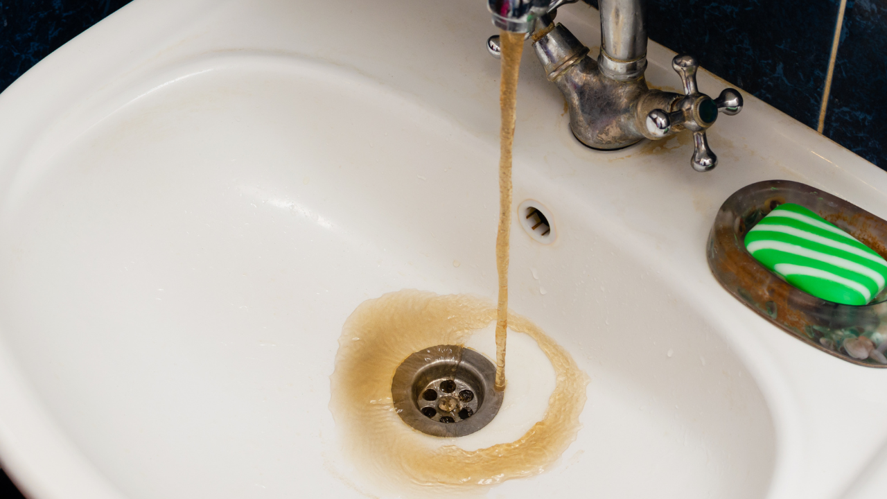 Dirty brown water running from a faucet into a white sink with a green soap dish nearby