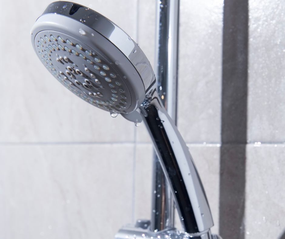 Chrome showerhead spraying water in a tiled bathroom Chrome showerhead spraying water in a tiled bathroom