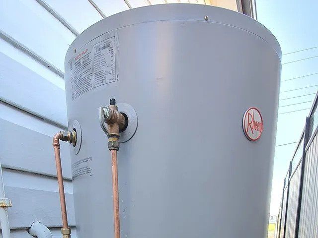 Large gray water heater tank with copper pipes in a utility room