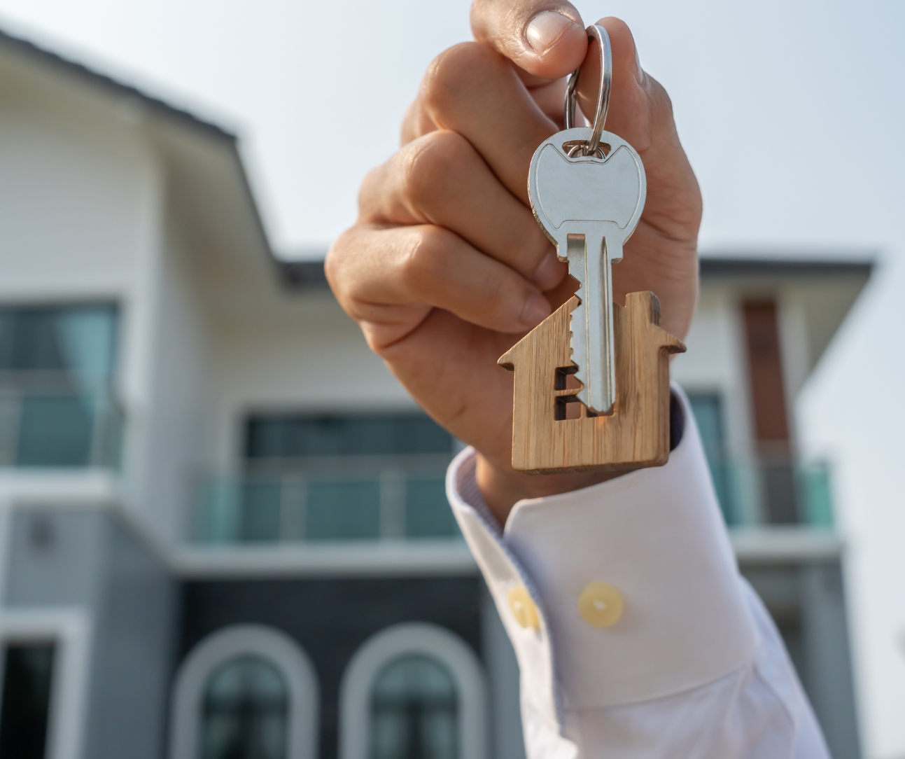 Hand holding house-shaped keychain in front of a modern home exterior