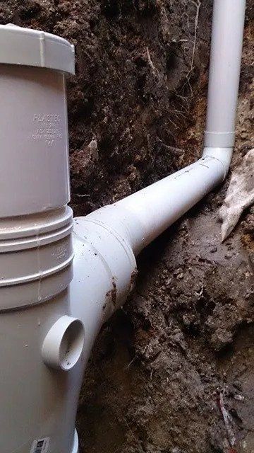 White PVC drainage pipes running through a dirt trench beside a wall