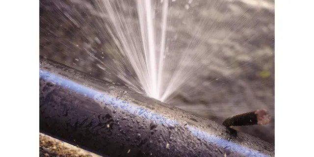 Close-up of a black pipe being sprayed with water, creating a fine mist and droplets.
