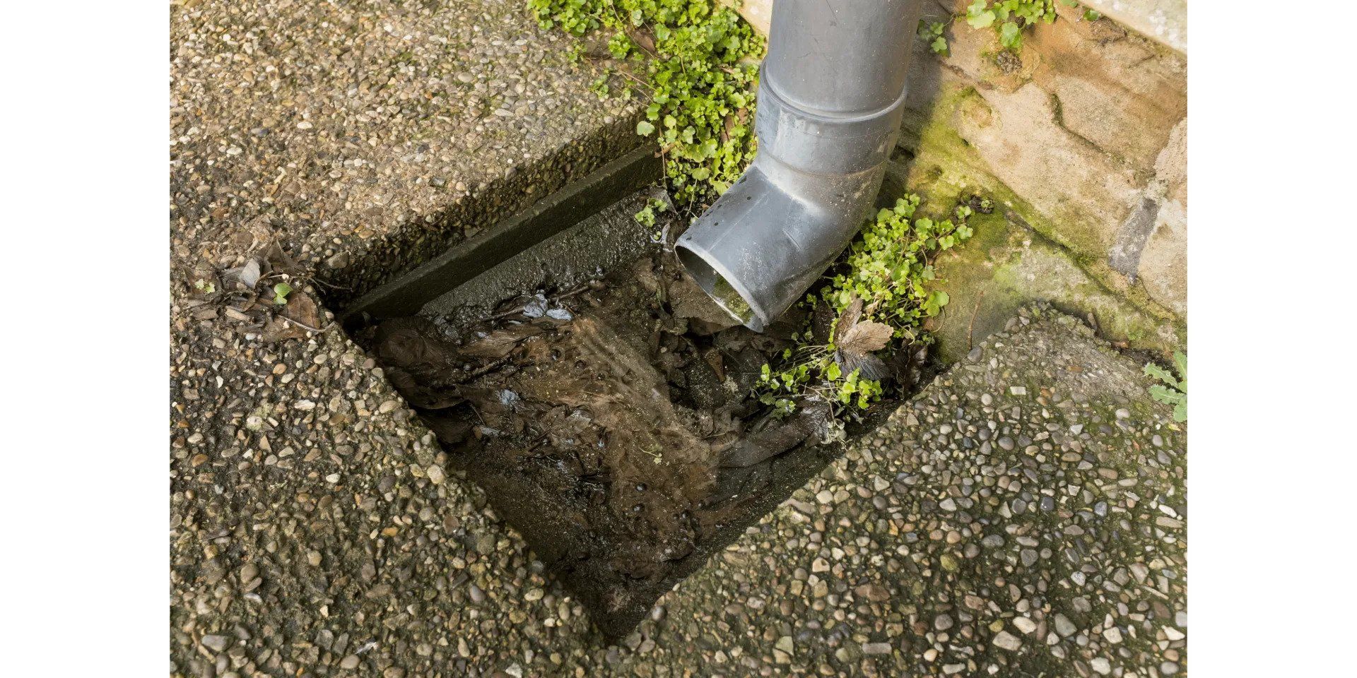 Gutter downspout draining rainwater into a gravel-lined drain pit beside a stone wall