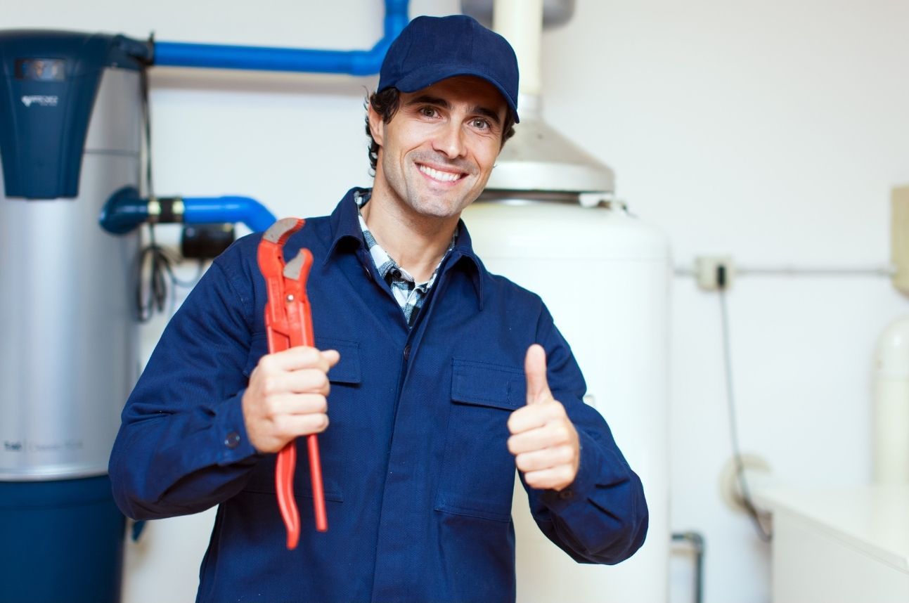 Smiling worker in blue uniform and cap holding red pliers and giving a thumbs-up in an industrial room