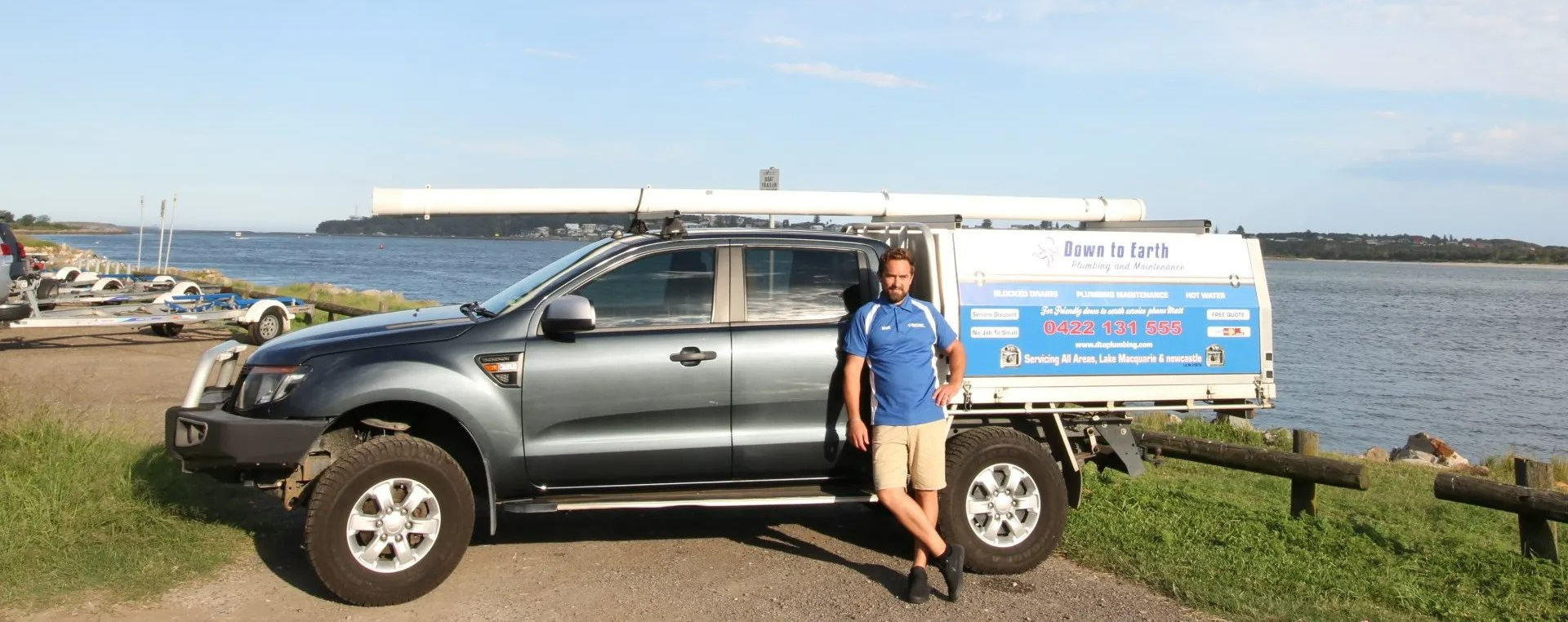Person standing by a gray pickup truck with a blue trailer at a waterfront harbor