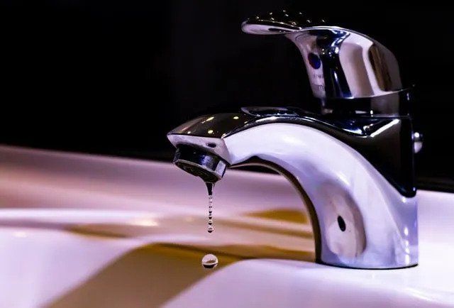 Chrome faucet dripping water into a white sink.