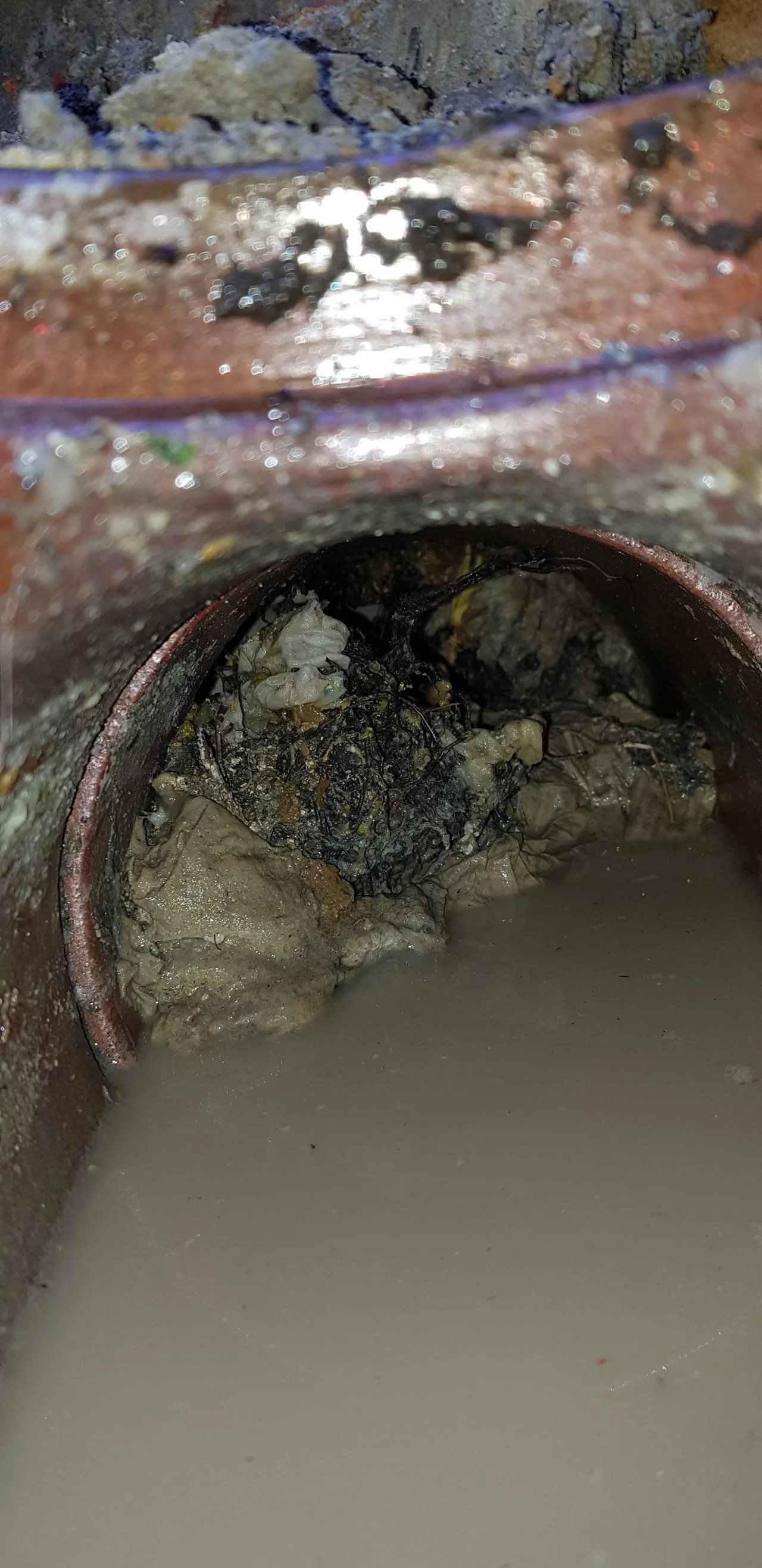 Rusty metal pipe opening with murky water and debris inside