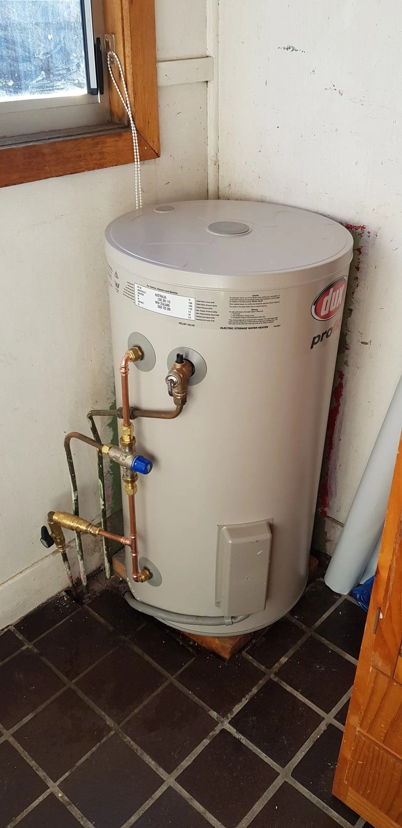 White water heater with exposed pipes in a small tiled utility room