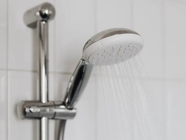 Chrome shower head spraying water in a tiled bathroom