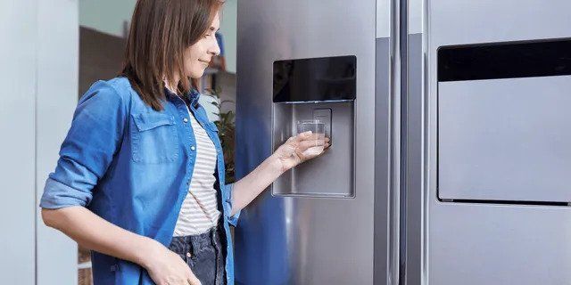 Woman using a built-in refrigerator dispenser in a modern kitchen