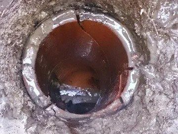 A rusted circular pipe opening in concrete, with dark water or debris inside.