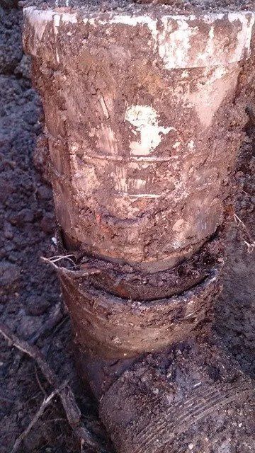 Close-up of a rusted metal pipe or valve emerging from muddy ground with white residue on top