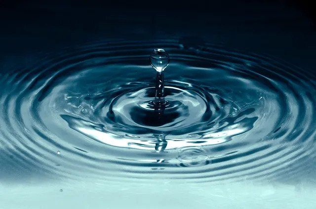 Water droplet splashing into a blue surface, creating concentric ripples