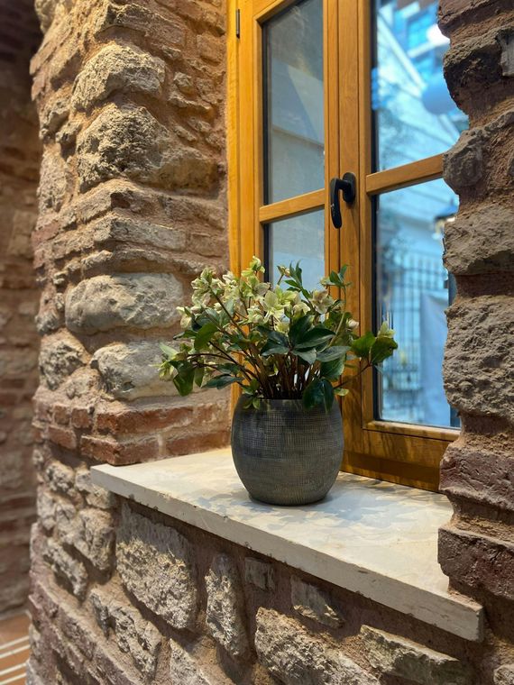 Stone wall with a wooden framed window; a potted plant sits on the window sill.