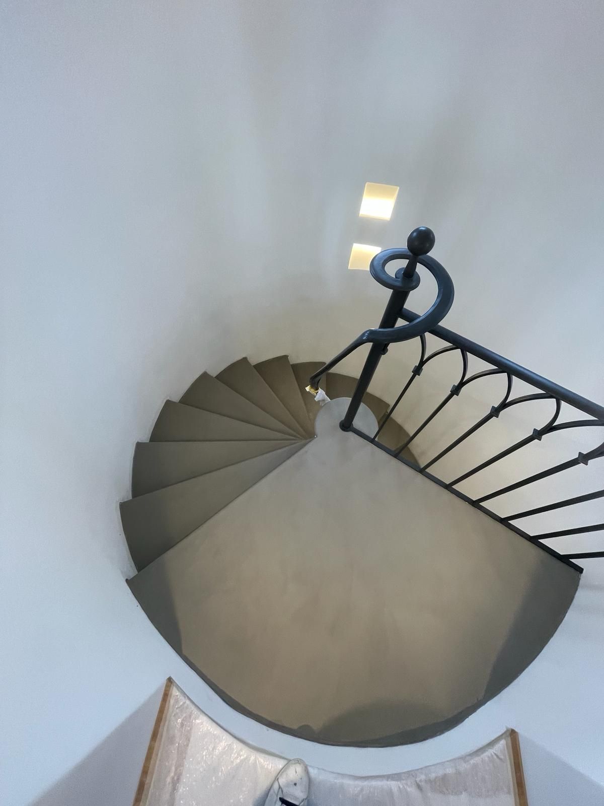 Escalier en colimaçon avec rampe sombre dans un intérieur blanc, vu de dessus.