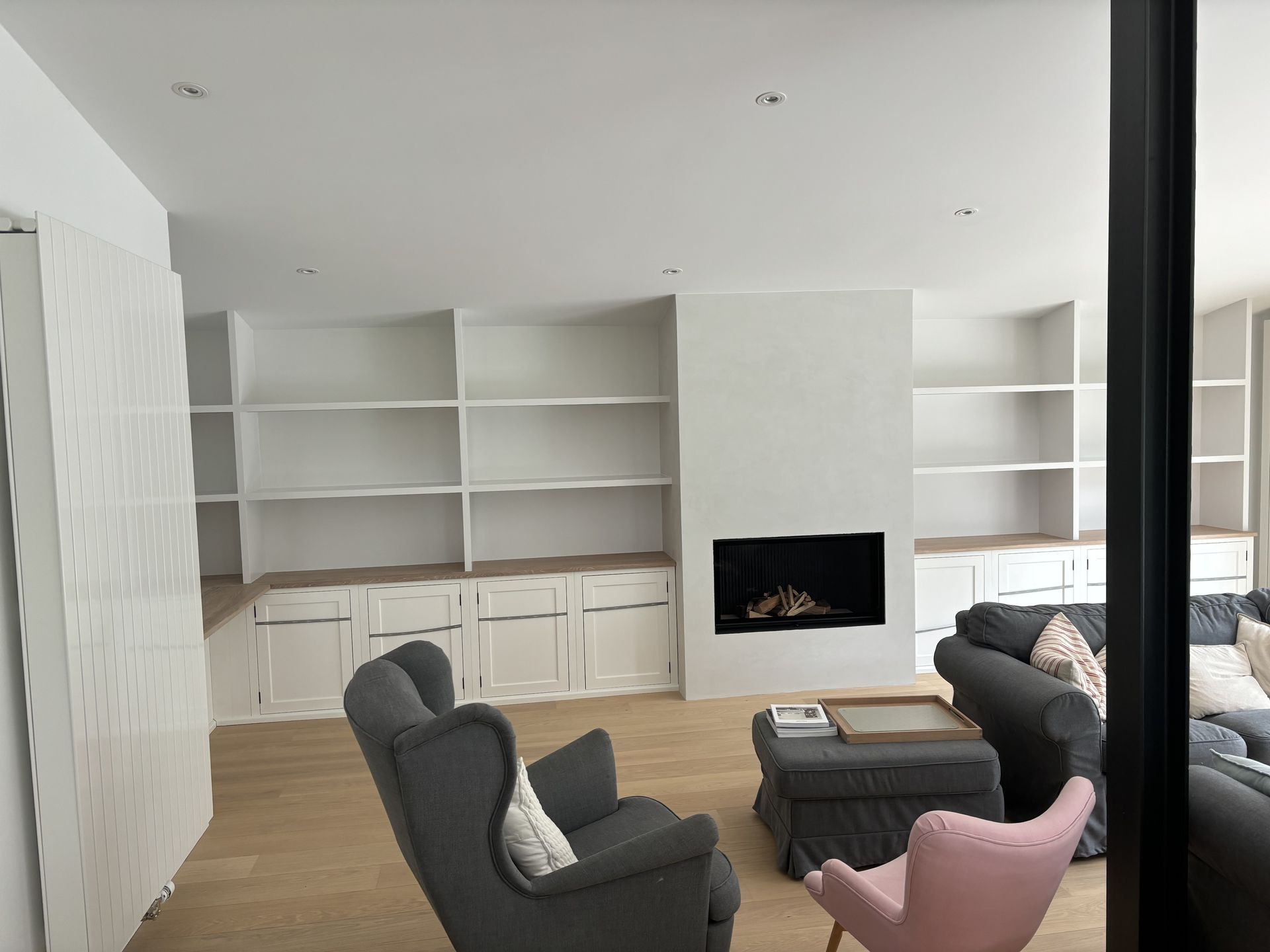Salon moderne avec étagères intégrées, cheminée et chaises grises et roses