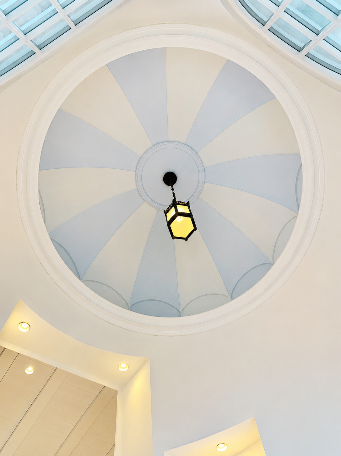 Dôme au plafond orné de panneaux bleu pâle et crème et d'une lanterne suspendue dans un intérieur lumineux